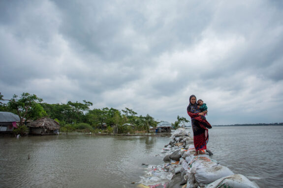 Woman and children walk over sandbag embankment in Bangladesh.